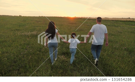 happy family walking sunset park, boy child father mother holding hands together walking green meadow, little son boy parents picnic, walk field sunset, view from back, man woman child holding hand 131654286