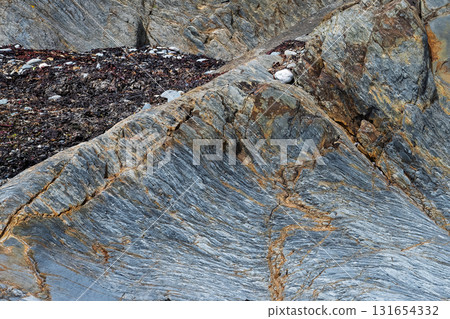 Exposed rock formations reveal distinct layers in blue, grey, and gold. Located on the coast in West Cork, Ireland, the textures and colors create an interesting geological study. Exposed rock formations reveal distinct layers in blue, grey, and gold. Located on the coast in West Cork, Ireland, the textures and colors create an interesting geological study. 131654332