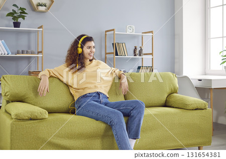 Attractive young woman in headphones sitting on sofa at home Attractive young woman in headphones sitting on sofa at home 131654381