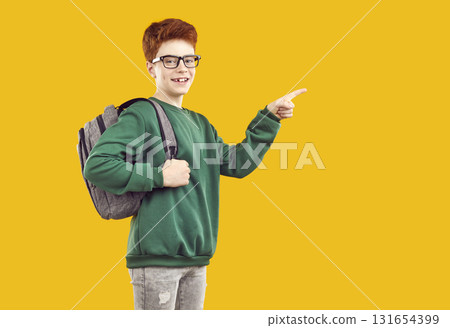 Happy school child advertising something and pointing to side on yellow background Happy school child advertising something and pointing to side on yellow background 131654399