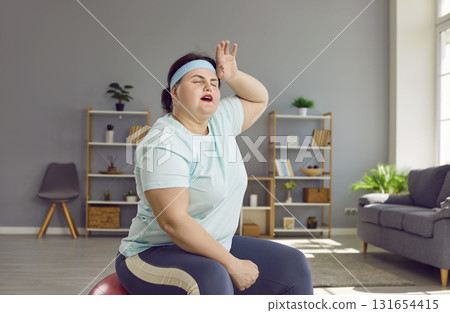 Tired overweight woman wipes sweat off her forehead after a sports workout at home 131654415