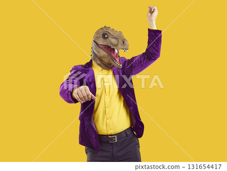 Man in purple suit and funny dinosaur mask dancing gangnam style on yellow background 131654417