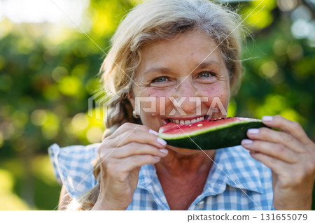 Lovely senior woman eating slice of watermelon in garden. 131655079