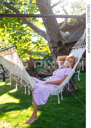 Older woman lying in a hammock and resting, quiet time in garden. 131655081