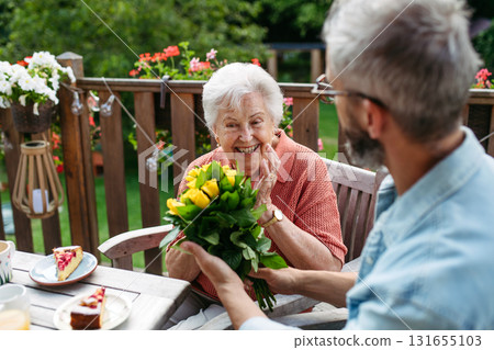 Mature bringing bringing flowers to his old mother. Mature bringing bringing flowers to his old mother. 131655103