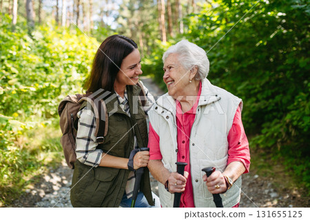 Senior woman and daughter enjoying hike with trekking poles. 131655125