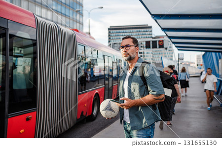 Handsome man boarding bus, holding sport ball and phone. 131655130
