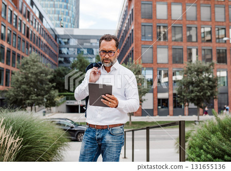 Businessman in front of office building, holding tablet and reading something. 131655136