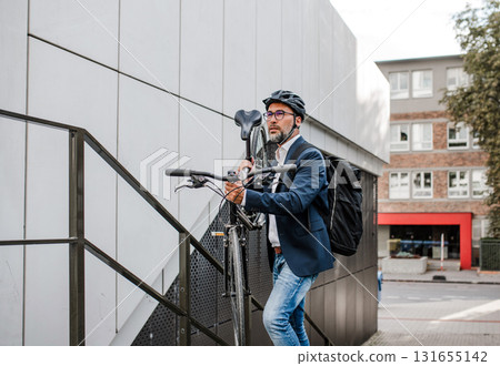 City commuter carrying bicycle up urban stairs. 131655142
