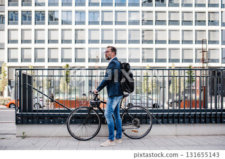 City commuter walking with bike to office, wearing backpack and helmet. 131655143