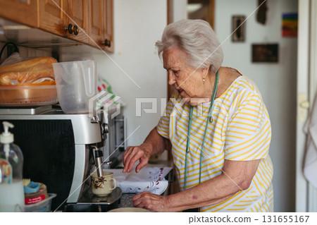 Elderly lady making coffee in coffee maker at morning. Elderly lady making coffee in coffee maker at morning. 131655167