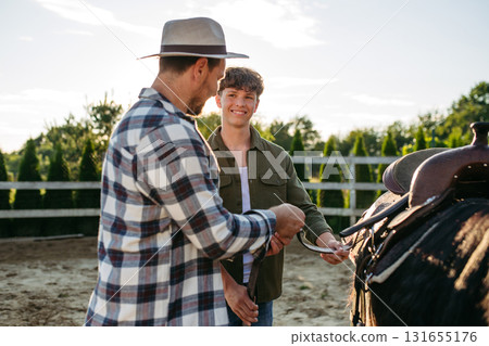 ather and son preparing horse for riding. ather and son preparing horse for riding. 131655176