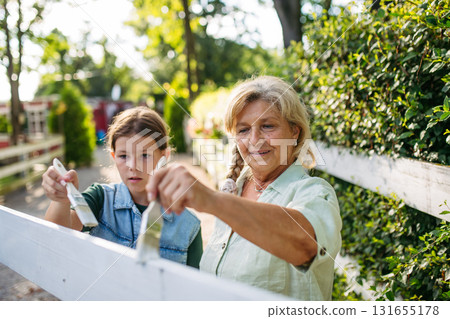 Young girl helping on farm, painting fence. 131655178