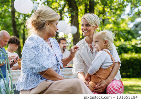 Smiling grandmother talking with her daughter, holding grandchild, family gathering. Smiling grandmother talking with her daughter, holding grandchild, family gathering. 131655184