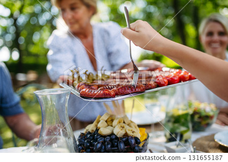 Senior woman serving grilled food during family grill party. Senior woman serving grilled food during family grill party. 131655187