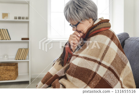 Senior woman sitting on sofa at home wrapped in a blanket feeling unhealthy with influenza Senior woman sitting on sofa at home wrapped in a blanket feeling unhealthy with influenza 131655516