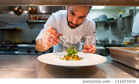 Chef meticulously plating a gourmet dish with tweezers in a professional kitchen setting for fine dining 131655620