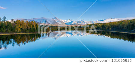 Tranquil mountain lake mirrors snow capped peaks and pine forest under a blue sky 131655955