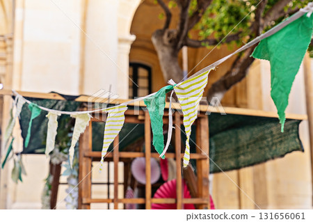 Close view of fabric bunting and pennant flags strung above market stall in urban courtyard, cheerful spring vibe Close view of fabric bunting and pennant flags strung above market stall in urban courtyard, cheerful spring vibe 131656061