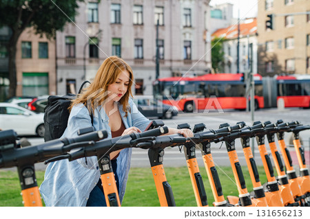 Curvy woman unlocking shared e-scooter in city. 131656213