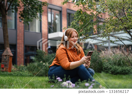 Confident woman relaxing, listening podcast outdoors in park. 131656217