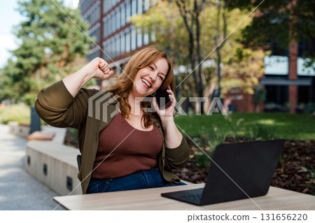 Plus size woman working remotely from coffee shop, making phone call with client. Plus size woman working remotely from coffee shop, making phone call with client. 131656220