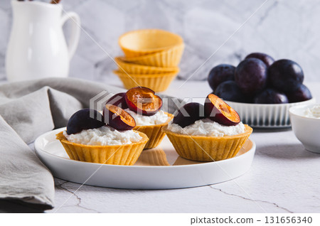 Mini tartlets with cottage cheese and plum on a plate on the table 131656340