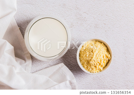 Close up of colostrum powder in a bowl and a drink in a glass on a table top view Close up of colostrum powder in a bowl and a drink in a glass on a table top view 131656354