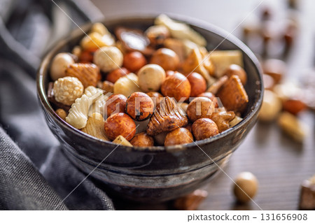 Salted snack. Coated peanuts and mini crackers in bowl on wooden table. 131656908