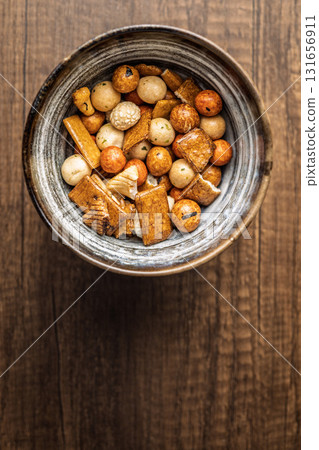 Salted snack. Coated peanuts and mini crackers in bowl on wooden table. 131656911