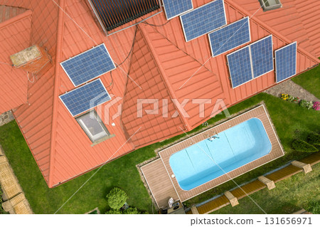 Aerial view of a new autonomous house with solar panels and water heating radiators on the roof and green yard with blue swimming pool. 131656971