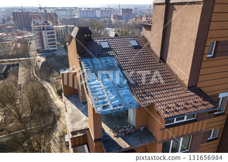 Aerial top view of unfinished tall apartment building, annex room under construction, high chimneys and plastic windows on tiled roof. Aerial top view of unfinished tall apartment building, annex room under construction, high chimneys and plastic windows on tiled roof. 131656984