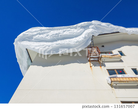 A clear blue sky and a large snow cornice jutting out from the roof of a hotel (Shiga Kogen, Nagano Prefecture) 131657007