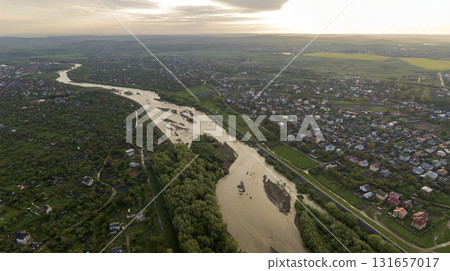 Aerial landscape of small town or village with rows of residential homes and green trees and big flloded river. 131657017