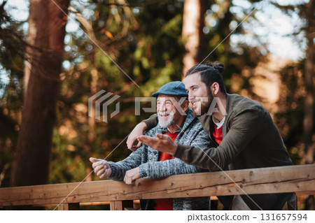Older father and his son standing on bridge, looking at nature. Older father and his son standing on bridge, looking at nature. 131657594