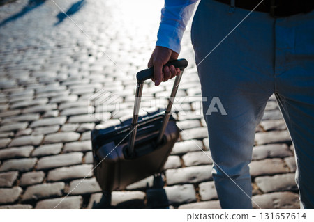 Businessman pulling suitcase on cobblestone street. 131657614