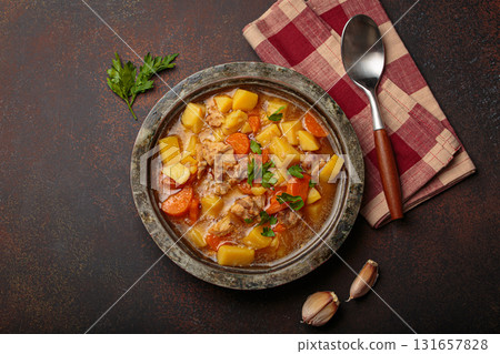 Chicken stew or soup with potatoes and carrots served in rustic bowl with spoon top view on dark brown concrete background 131657828