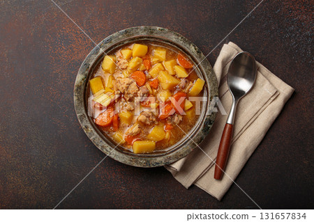 Chicken stew or soup with potatoes and carrots served in rustic bowl with spoon top view on dark brown concrete background Chicken stew or soup with potatoes and carrots served in rustic bowl with spoon top view on dark brown concrete background 131657834