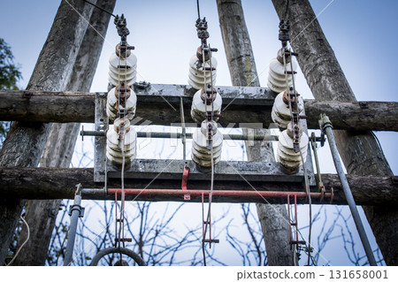 Old high-voltage ceramic electrical insulators mounted on wooden poles, part of a power distribution Old high-voltage ceramic electrical insulators mounted on wooden poles, part of a power distribution 131658001