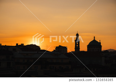 Cityscape of Bergamo, Italy at sunset with silhouettes of historical buildings and church domes against a golden orange sky Cityscape of Bergamo, Italy at sunset with silhouettes of historical buildings and church domes against a golden orange sky 131658165