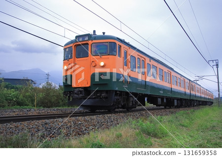 Shinano Railway 115 series train (Shonan color) running through Karuizawa on a cloudy day, watched over by Mount Asama. Photographed on October 4, 2025. Shinano Railway 115 series train (Shonan color) running through Karuizawa on a cloudy day, watched over by Mount Asama. Photographed on October 4, 2025. 131659358