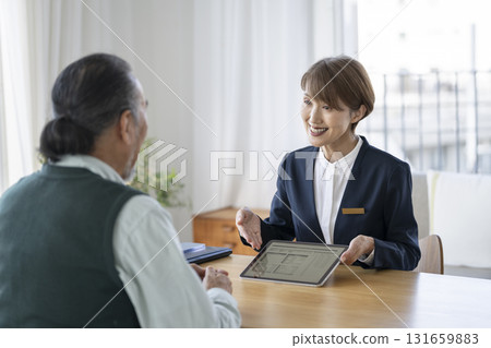 A businesswoman talking to a senior man while showing him documents on a tablet 131659883