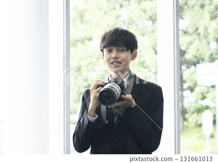 Man in a suit holding a camera 131661013