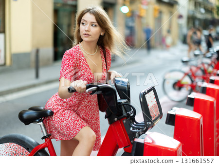 young woman stands near a bicycle rental point young woman stands near a bicycle rental point 131661557