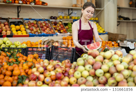 Female salesman in an apron carefully places ripe watermelons on supermarket counter 131661856
