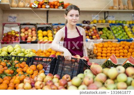Female salesman in an apron carefully places ripe apples on supermarket counter Female salesman in an apron carefully places ripe apples on supermarket counter 131661877