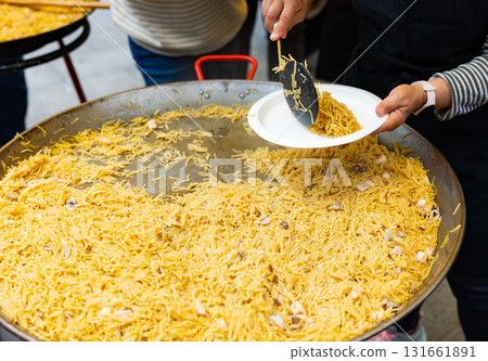Cook serving into plates fideua with seafood prepared at street holiday 131661891