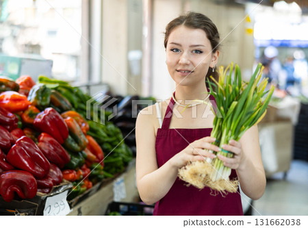 Young woman seller offering onions in vegetable shop Young woman seller offering onions in vegetable shop 131662038