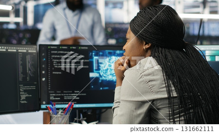 Server room specialist applies artificial intelligence technology to minimize system downtime. African American worker develops and deploys AI solutions to optimize data center equipment, camera B 131662111
