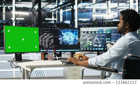 Data center admin in wheelchair using AI node tree software on green screen PC to minimize system downtime. Server hub employee in disability using visual programming tool on mockup computer, camera B 131662117